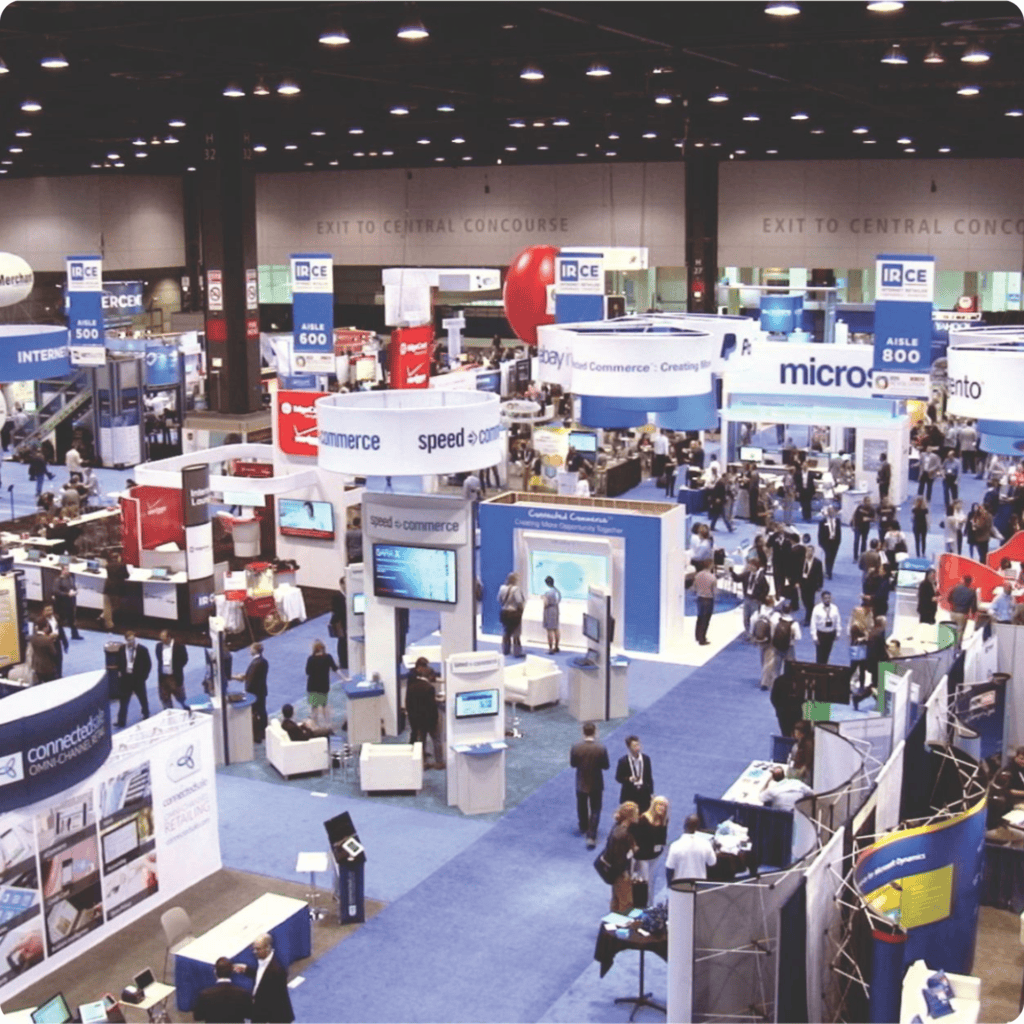Busy trade show with numerous booths and visitors at a large conference event.